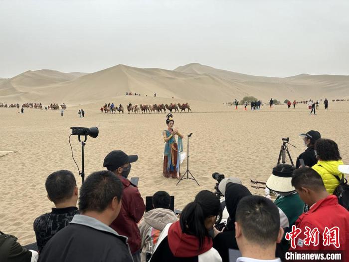 圖為2023年4月底，敦煌大漠“逐舞者”奧楠在鳴沙山月牙泉景區(qū)視頻直播，吸引游人圍觀。　馮志軍 攝